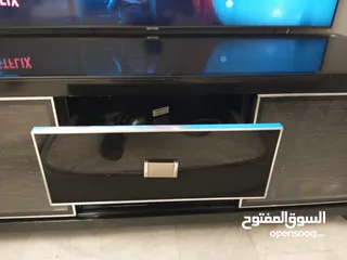  8 طاولة تلفزيون لون اسون بحالة ممتازة للبيع درجين وسطانيات واماكن تخزين جانبية  سطح زجاجي وارفف زجاجية