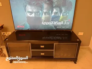  1 طاولة تلفزيون لون اسون بحالة ممتازة للبيع درجين وسطانيات واماكن تخزين جانبية  سطح زجاجي وارفف زجاجية