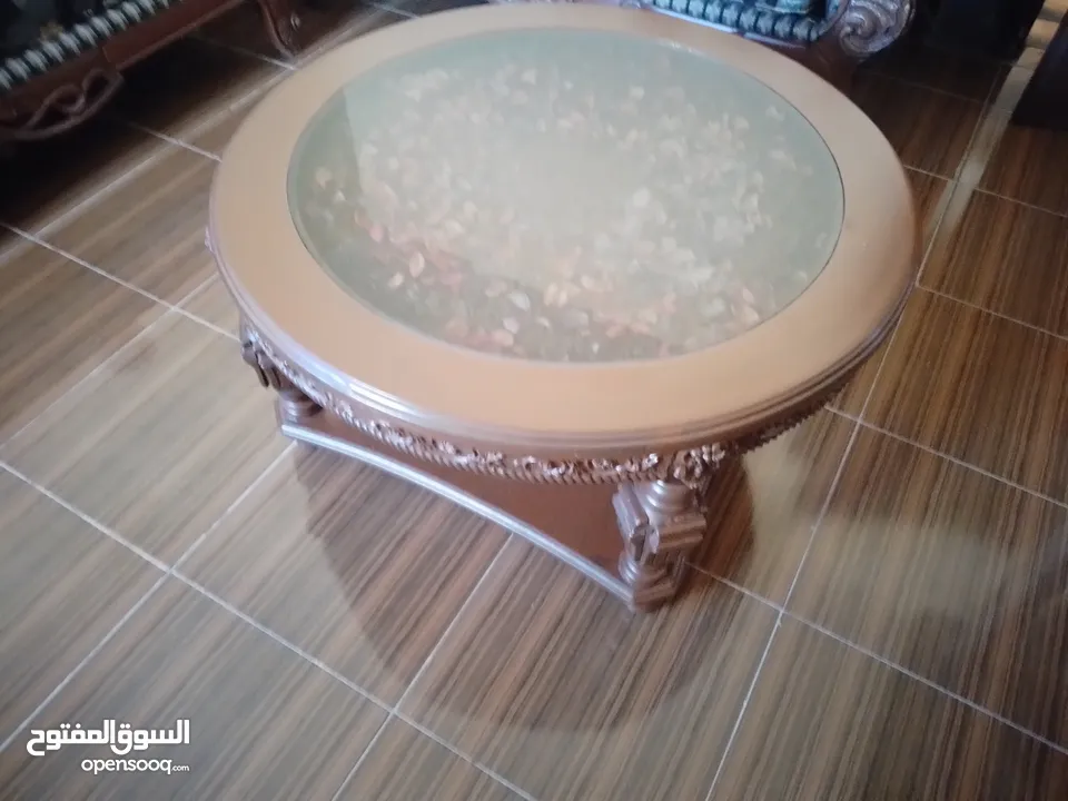 غرفة جلوس مع ثلاث طاولات واحدة كبيرة في الوسط واثنتين وسط مع طاولة كزاز كبيرة وكرسيين خشب