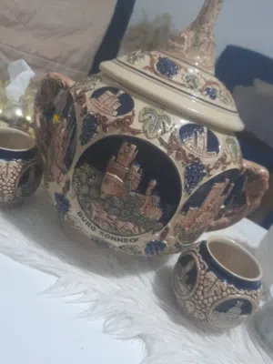 للبيع قطعة خزفية ألمانية قديمة مميزة مع غطاء وكأسين أصليين. تحمل رسومات بارزة لمعالم المانيه