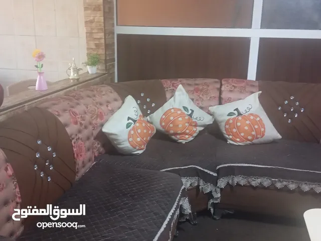 طقم كنب كورنر باللون البني مع كفر لون بني وطاوله وسط باللون البيج وثلاث طاولات سيرفس